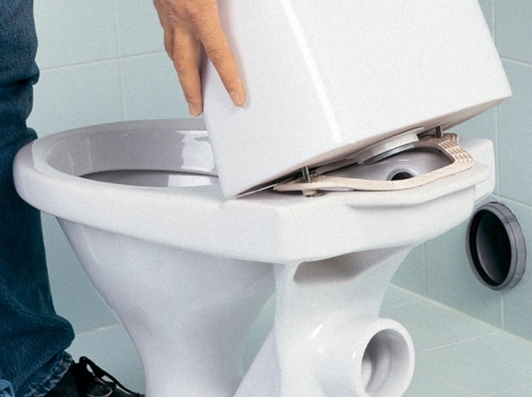 Мастер снимает бачок унитаза